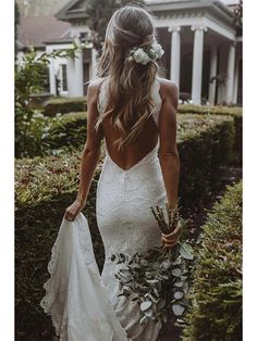 the back of a woman in a white wedding dress holding a bouquet and looking down