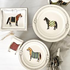 three plates with horses painted on them are next to silverware and utensils