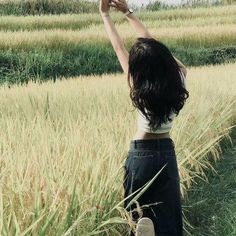 a woman standing in the middle of a field holding an umbrella over her head with both hands