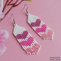 the pink and white beaded earrings are next to a flower on a pink surface