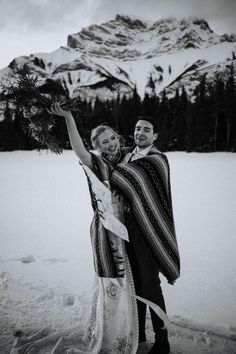 a man and woman are standing in the snow with their arms around each other holding flowers