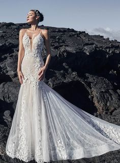 a woman standing on top of a rocky hillside wearing a wedding dress with an open back