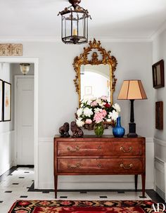 a dresser with flowers on top and a mirror above it in a room that is decorated with black and white checkered floor tiles