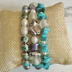 Stack them up or choose individual pieces! All three bracelets are size 6 3/4" stretch bracelets. Bracelet 1-This bracelet features spotted turquoise jasper beads, renowned for their earthy hues and unique patterns. Each bead features stainless steel caps. The perfect contrast to the rustic turquoise and silver is the freshwater pearl focals. Bracelet 2 a captivating fusion of eclectic elements and artisan craftsmanship. At the heart of this exquisite piece is a large gray freeform pearl. Complementing the gray pearl are large amethyst wheels with varying depth of purple, small freshwater white pearls and gray pearls. Lastly, there are semi-transparent clear color African recycled glass to add cultural depth. Bracelet 3 is made of varying sizes of Howlite Turquoise pieces separated by clea Bohemian Turquoise Glass Bracelets, Turquoise Polished Bohemian Beads, Turquoise Gemstone Crystal Bracelet, Bohemian Style, Bohemian Turquoise Beaded Nickel-free Bracelets, Turquoise Multi-strand Bohemian Beads, Earthy Hues, Howlite Bracelet, Recycled Glass Bead, Turquoise Howlite