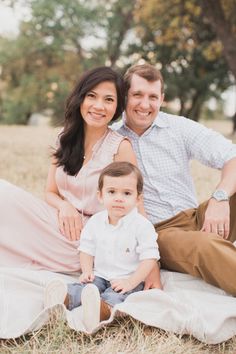 a man and woman sitting on top of a blanket next to a small boy in a field