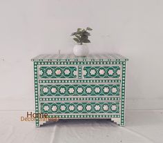 a white vase sitting on top of a green and white dresser next to a plant