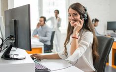 a woman sitting in front of a computer with headphones on while talking on the phone