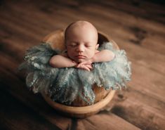 a baby is sleeping in a basket with blue feathers on it's head and arms