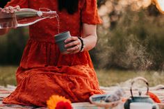 a woman in an orange dress pouring water into a cup on top of a blanket