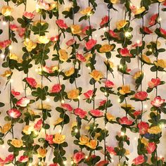 flowers and lights are hanging on the wall in front of a white backdrop with red, yellow and green leaves