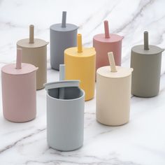 many different colored cups on a white marble surface with straw sticking out of one cup