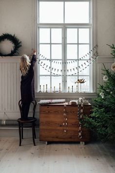 a woman standing next to a christmas tree in front of a window with bunting