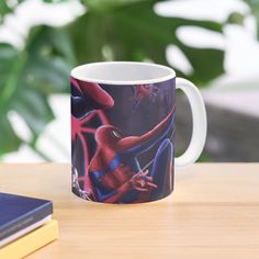 a spider - man mug sitting on top of a wooden table next to a book