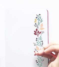 a hand holding a pen and writing on an open notebook with floral designs in it