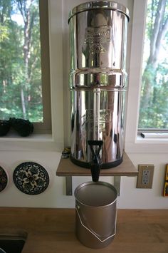 a coffee maker sitting on top of a wooden table next to a window with trees in the background