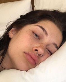 a woman laying in bed with her nose piercings tucked under her nose and nose ring