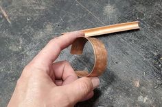 a hand holding a piece of wood in front of a metal object on the ground