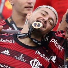 a man with a gold medal in his mouth is surrounded by other men who are wearing red and black shirts