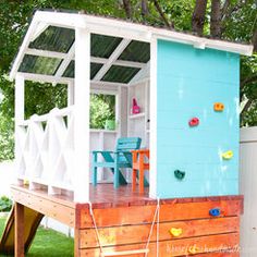 a small blue and white house with a wooden deck in the grass next to a tree