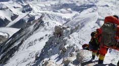 two climbers climbing up the side of a snow covered mountain