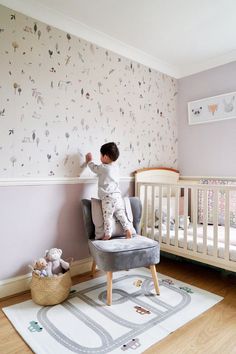 a small child standing on top of a chair next to a crib in a room