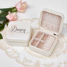 an open jewelry box sitting on top of a table next to pink roses and flowers