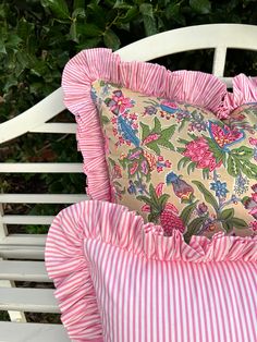 a pink and white pillow sitting on top of a wooden bench next to a bush