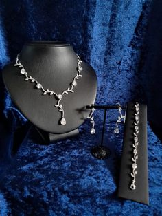 a necklace and earring set sitting on a blue velvet surface with jewelry in the foreground