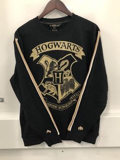 a harry potter sweatshirt hanging up on a white wall with the hogwarts logo