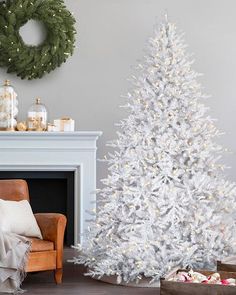 a white christmas tree sitting in front of a fireplace next to a chair and wreath