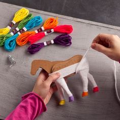 a person is holding a toy horse next to some colorful thread and scissors on a table