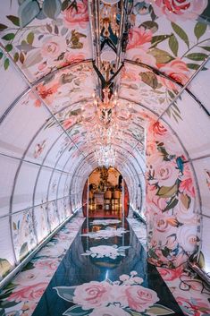 the inside of a glass tunnel decorated with flowers and chandelier hanging from it's ceiling