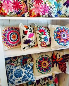 many colorful pillows are on display in a store shelf with white shelving and wooden shelves