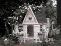 a doll house in the middle of a garden with flowers and trees around it,