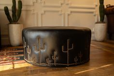 a black leather ottoman sitting on top of a wooden table next to cacti