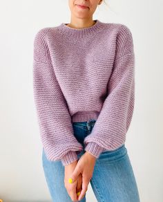 a woman in a purple sweater is posing for the camera with her hand on her hip