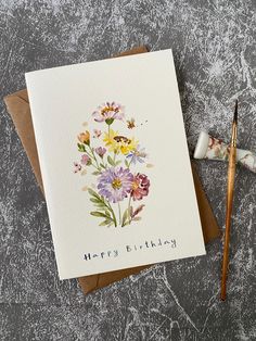 a birthday card with watercolor flowers on it next to a paintbrush and pencil