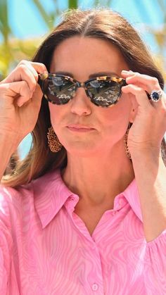 a woman in pink shirt holding up her sunglasses