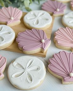 decorated cookies with pink and white icing sitting on a wooden board next to flowers