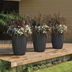 three large planters with flowers in them sitting on a wooden platform outside the house