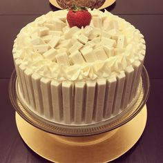 there is a cake with white frosting and a strawberry on the top, sitting on a gold plate