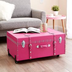 a pink suitcase sitting on top of a hard wood floor next to a gray couch