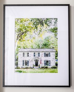 a white house with black shutters and trees in the background, framed on a wall