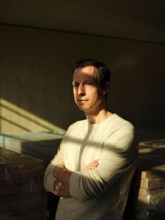 a man leaning against a wall with his arms crossed and looking at the camera while standing in front of stacks of boxes