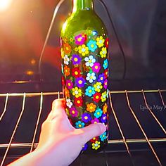 a hand is holding a colorful flowered bottle in front of an open oven door