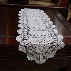 a table runner with white crocheted doily on it sitting on top of a wooden desk