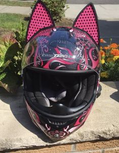 a motorcycle helmet with pink and black designs on the front is sitting next to flowers