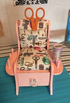 a chair with scissors and sewing supplies on it sitting on a table next to a spool of thread