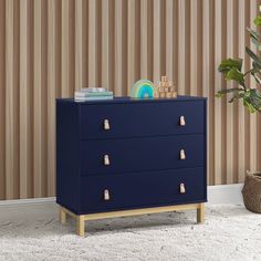 a blue dresser with gold handles in front of a striped wallpapered background and a potted plant