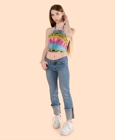 a young woman is posing in jeans and a tie dye top with her hands behind her head